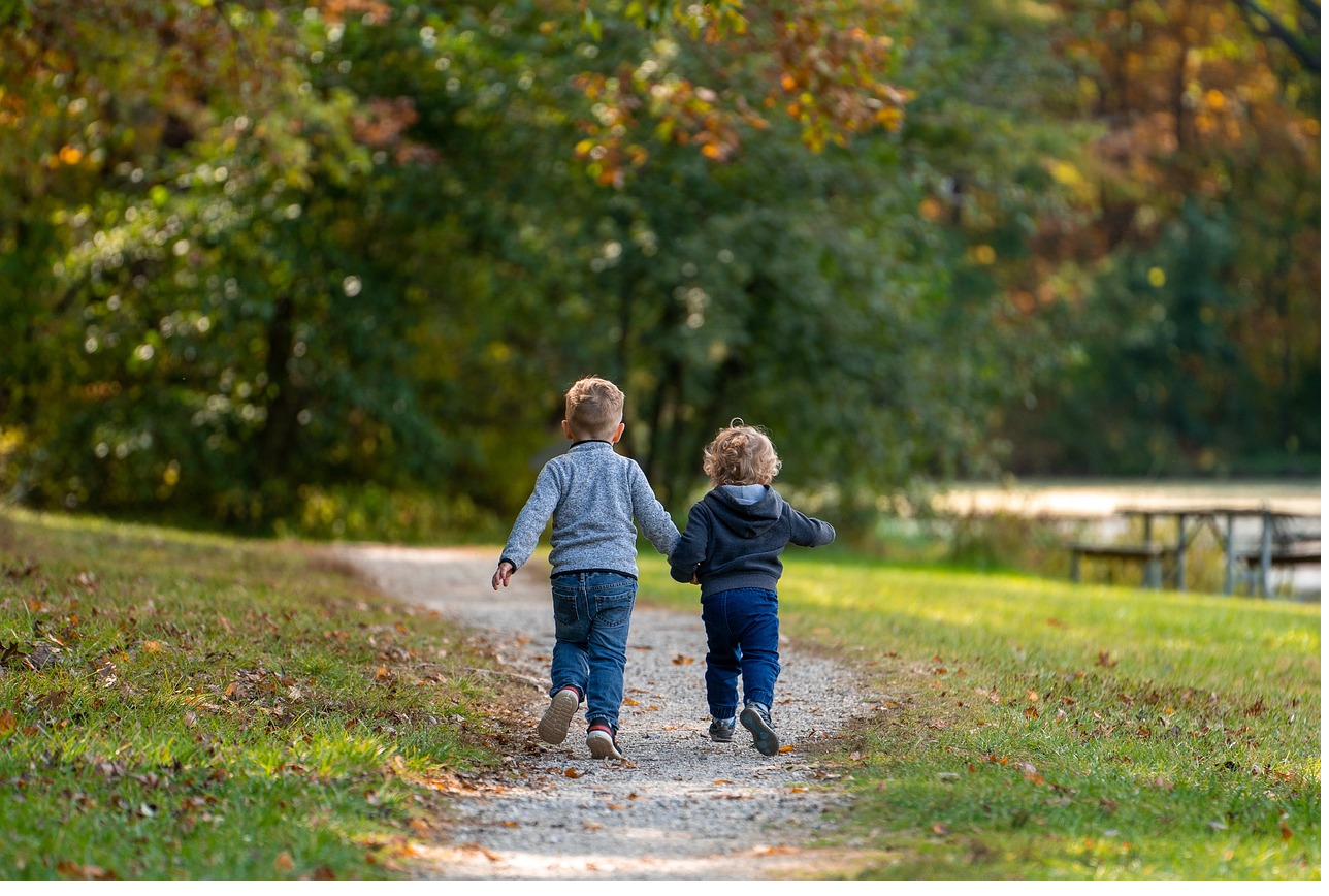 Two young children walking together on a forest path